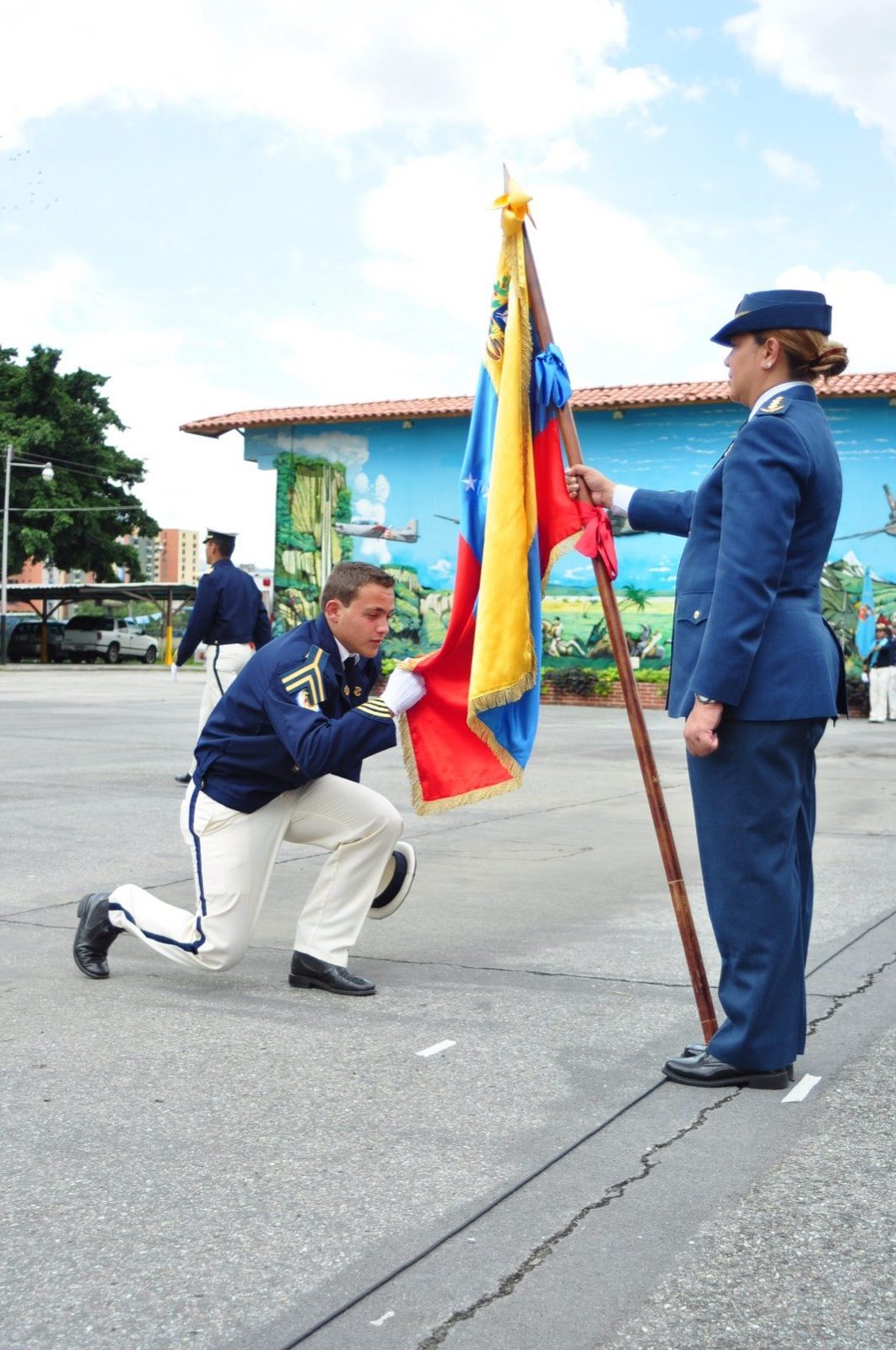 Cadete arrodillado besando la bandera nacional sostenida por la abanderada en el ósculo
